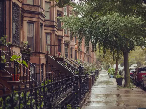Brownstones with stoops and iron railings along a rain-wet New York sidewalk
