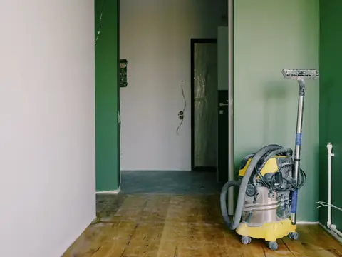A wet-dry vacuum standing in an empty room with bare wood floors