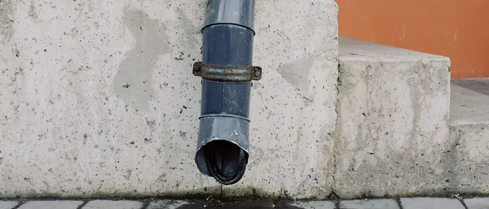A downspout ending above the paving at the foot of a wall
