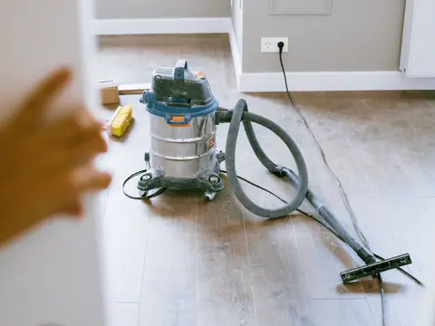 A wet-dry vacuum and its hose on the floor of a room under repair