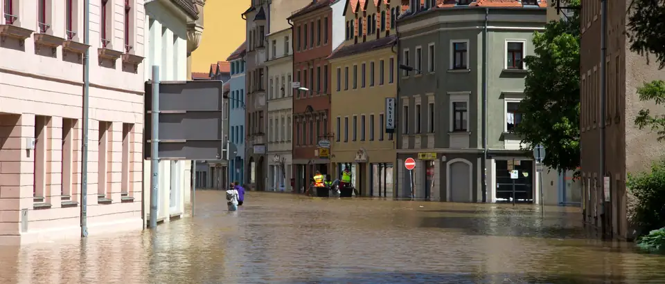A street of colorful row buildings standing in brown flood water on a sunny day