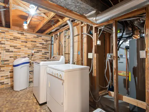 A basement with a water heater, laundry machines and open framing