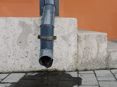 Rainwater dripping from the end of a downspout onto paving