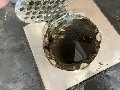 A hand lifting the strainer off a clogged floor drain