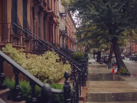 A rain-wet New York sidewalk lined with brownstones and trees