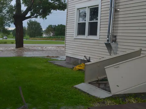 Flash flood water pooling in a yard beside a house and its outside cellar door